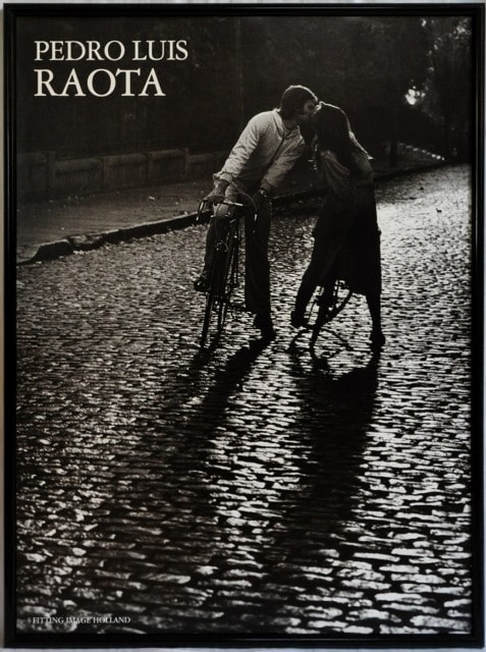 Poster of photograph by Pedro Luis Raota of a couple kissing while straddled on their bicycles