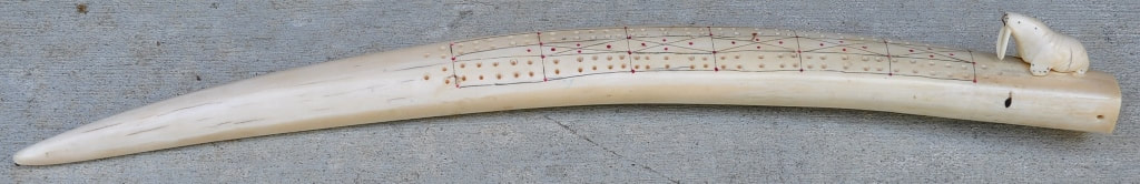 Alaskan walrus tusk cribbage board mounted with a carved walrus figurine