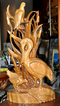 Carved wooden sculpture of stork and other birds in a grassland